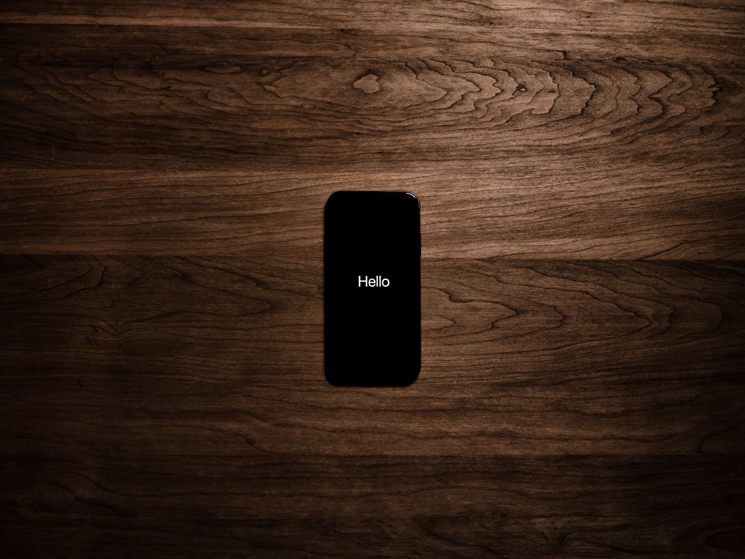 Black iphone screen with the word 'hello' across the screen on a brown table